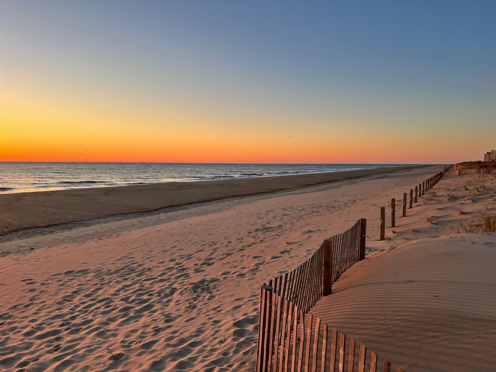 Sunset over a quiet sandy Ocean City beach, dunes, and wooden beach fencing